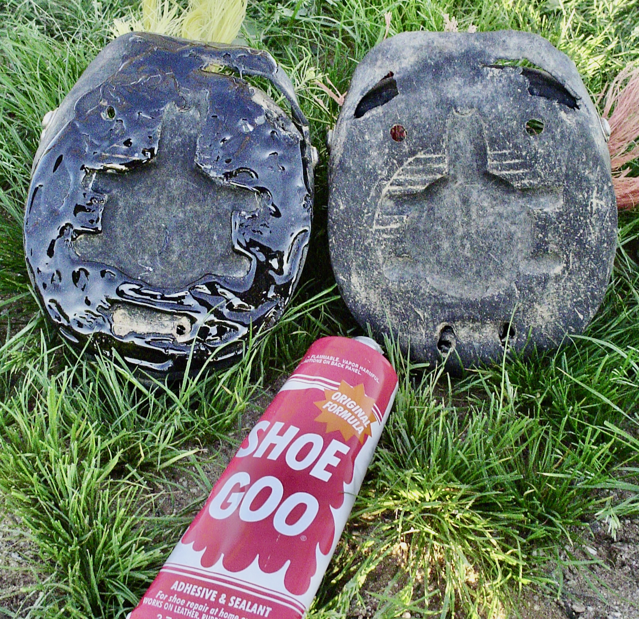 Two worn hoof boots on the grass, one patched with Shoe Goo, beside a tube of Shoe Goo